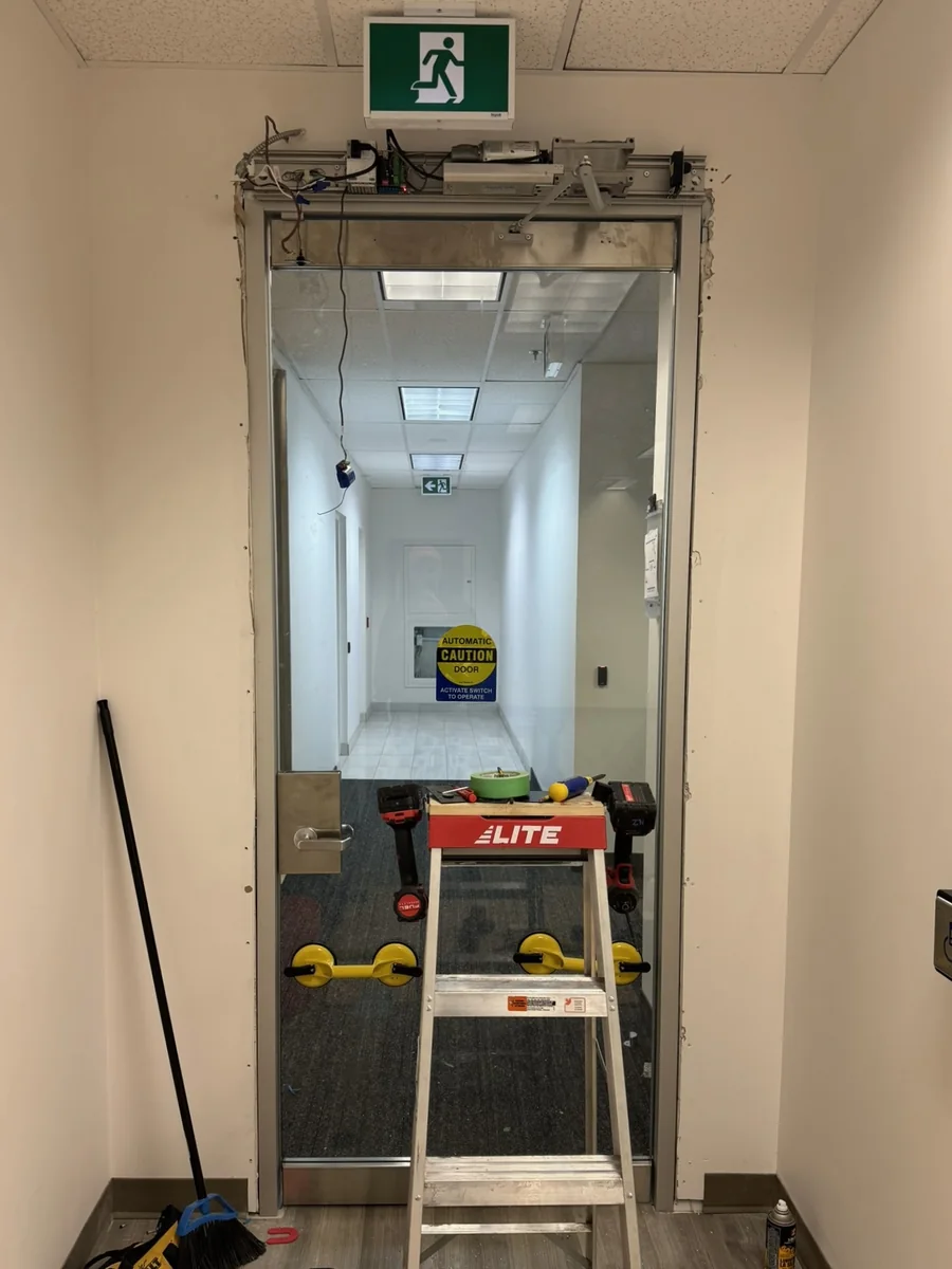 Automatic swing door operator exposed during repair while a new glass door is installed