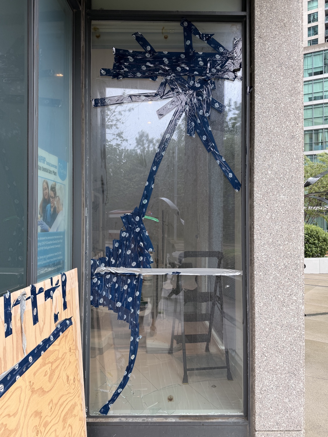 Broken storefront glass temporarily secured with tape before replacement
